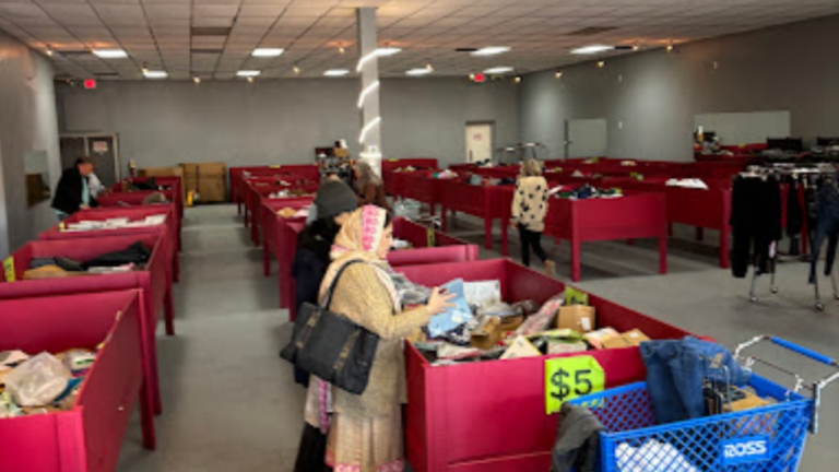 Shoppers browsing through red bins filled with assorted merchandise in a bin store with a $5 price sign visible on the front bin.