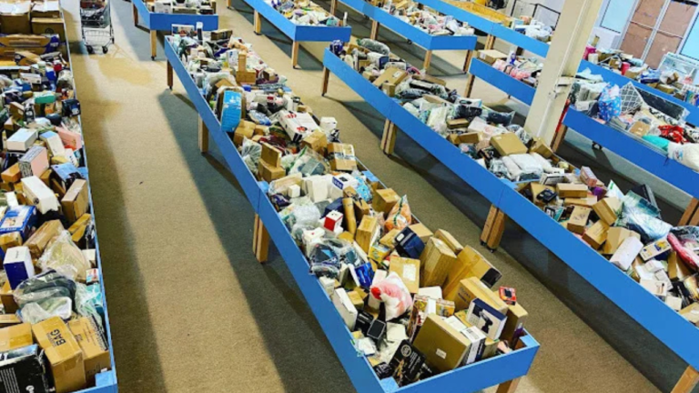 Rows of blue bins filled with assorted boxed and packaged merchandise in a brightly lit bin store, viewed from an elevated angle.
