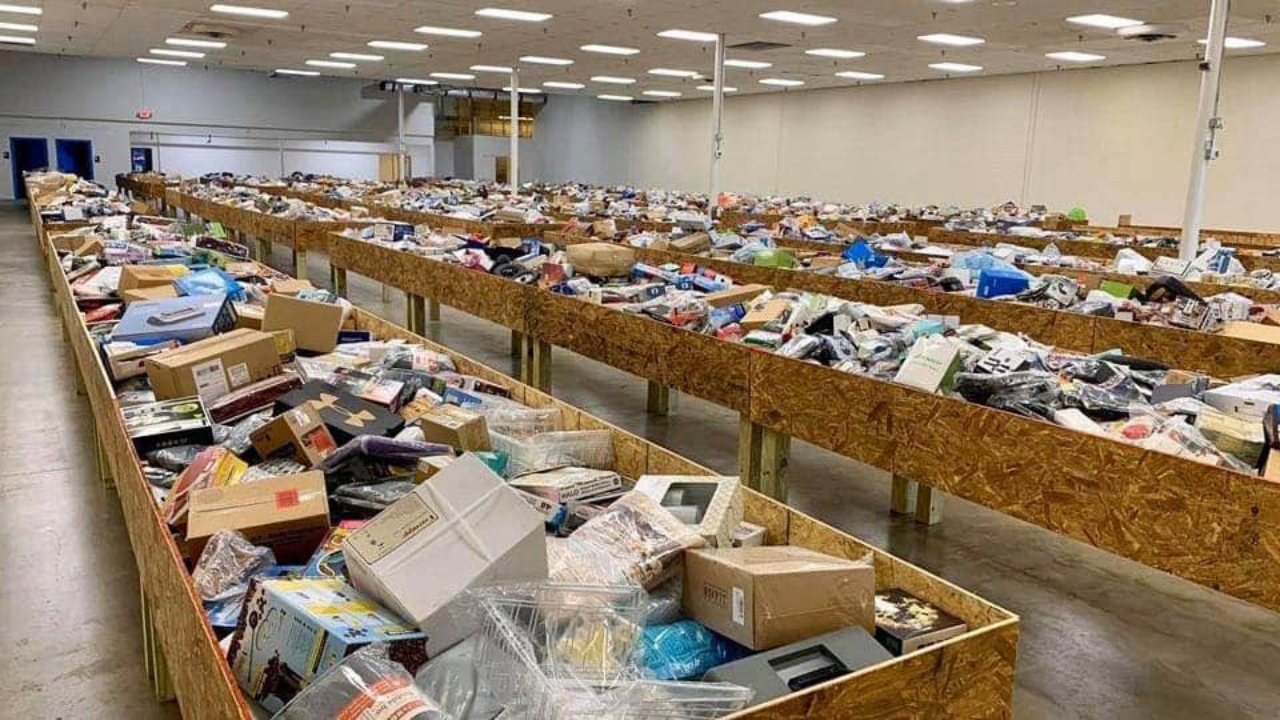 Interior of a large bin store with multiple rows of wooden bins filled with assorted liquidation and overstock items, including electronics, boxes, and household goods.