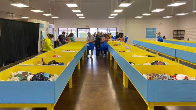 Shoppers browsing through organized yellow and blue bins filled with assorted items in a brightly lit bin store with polished brown floors."
