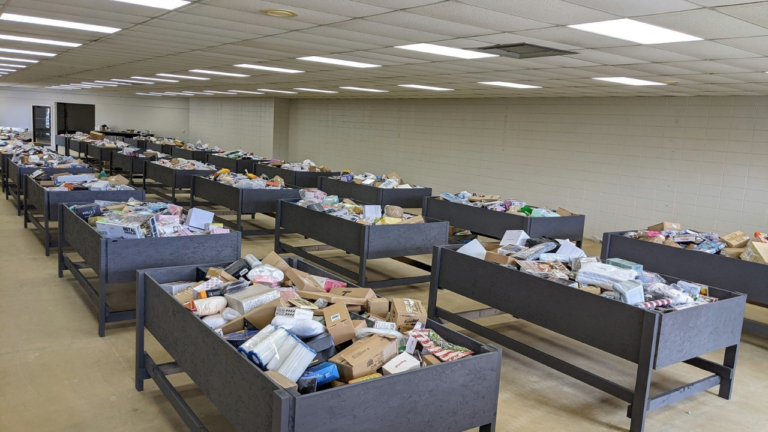 A spacious and well-lit bin store with multiple rows of large black wooden bins filled with assorted boxed and loose merchandise, creating an organized layout for bargain hunters to browse through discounted items.