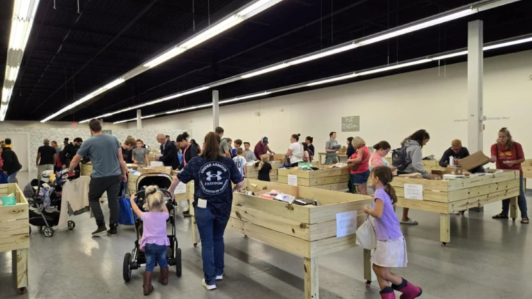 Families and individuals browse through wooden bins filled with discounted goods in a brightly lit bin store; several children are present, some pushing strollers, contributing to the family-friendly shopping atmosphere.
