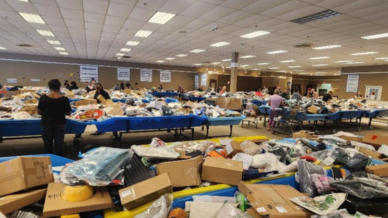 "Shoppers browsing through large blue bins filled with assorted merchandise, boxes, and products inside a spacious bin store with fluorescent lighting and signage indicating checkout and pricing."