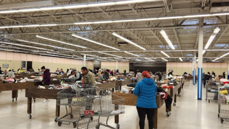 Shoppers browsing through large wooden bins filled with assorted items in a spacious, well-lit bin store, each person using shopping carts to collect their finds.