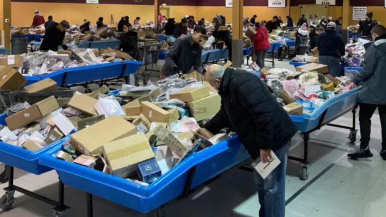 Shoppers browsing through large blue bins filled with assorted boxed and unboxed merchandise inside a busy bin store with fluorescent lighting.