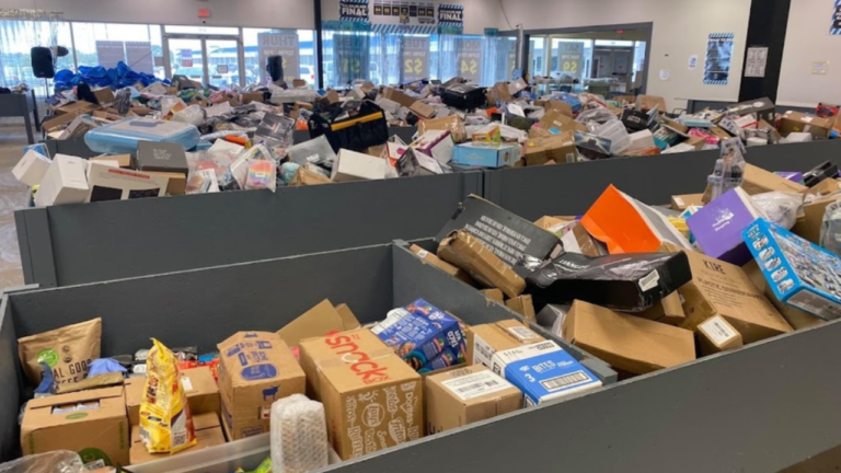 Shoppers browsing through large black bins filled with assorted discounted products, boxes, and merchandise inside a well-lit bin store.