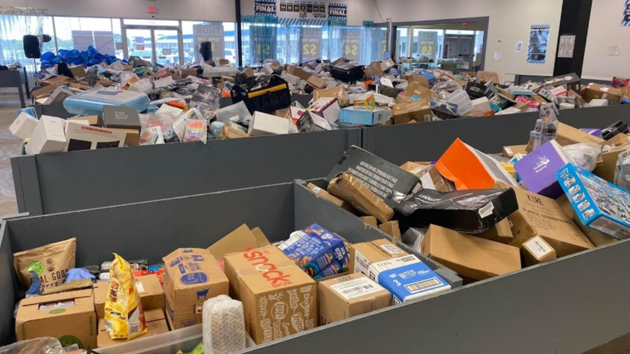 Shoppers browsing through large black bins filled with assorted discounted products, boxes, and merchandise inside a well-lit bin store.